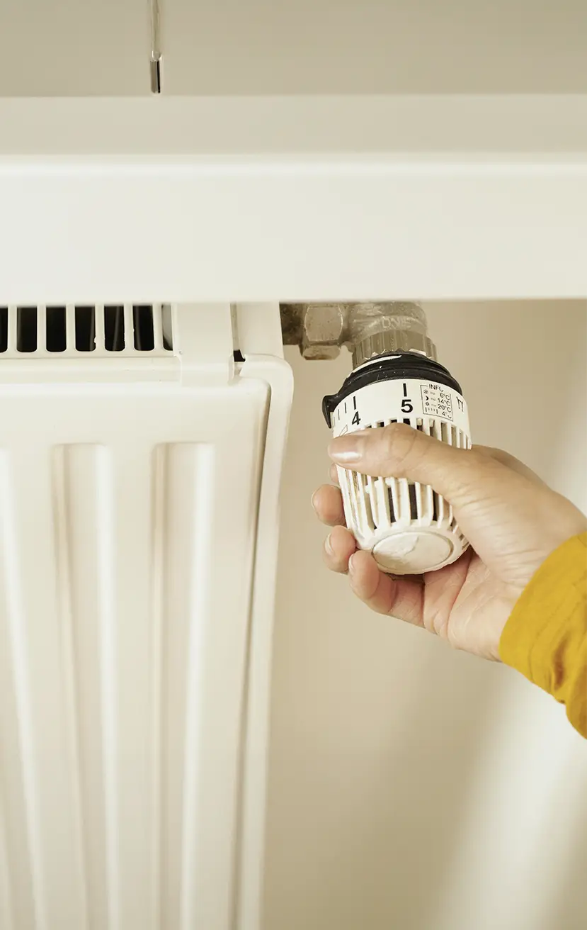Hand stellt das Thermostat an einem Heizkörper ein